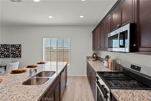 kitchen with stainless steel appliances, a sink, light wood-style floors, light stone counters, and dark brown cabinets