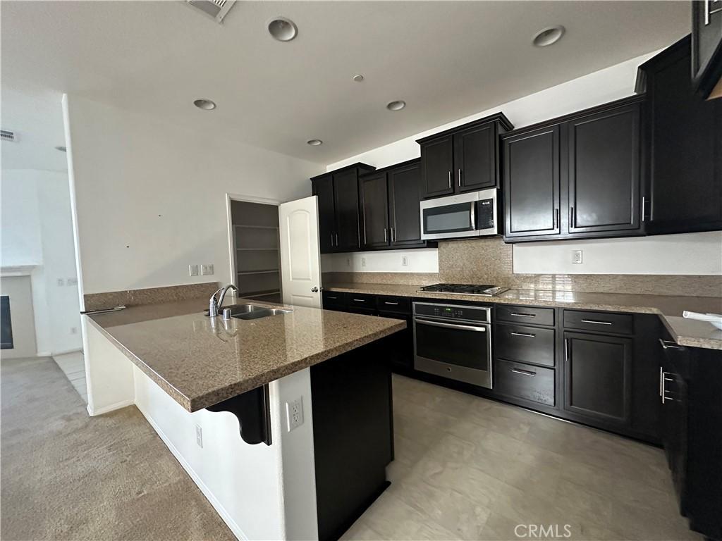 kitchen with stainless steel appliances, a sink, dark cabinetry, light stone countertops, and recessed lighting