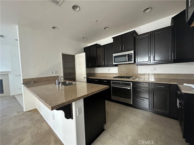 kitchen with stainless steel appliances, a sink, dark cabinetry, light stone countertops, and recessed lighting