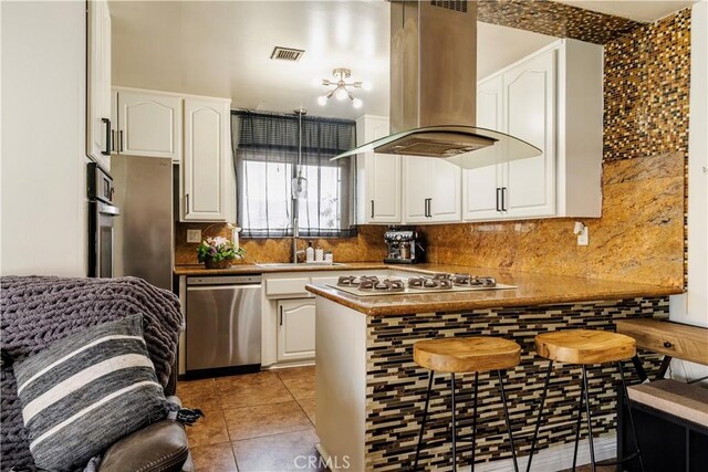 19264 Casmalia St, Rialto, CA 92377 - kitchen featuring island range hood, appliances with stainless steel finishes, white cabinetry, and decorative backsplash