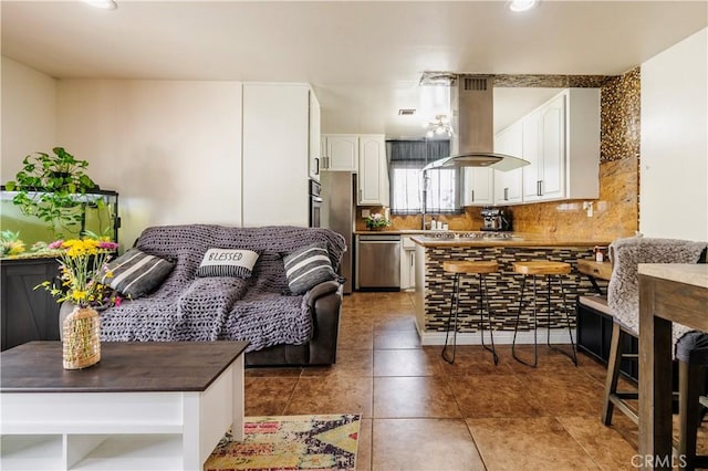 19264 Casmalia St, Rialto, CA 92377 - kitchen with island exhaust hood, appliances with stainless steel finishes, white cabinetry, tasteful backsplash, and light tile patterned floors