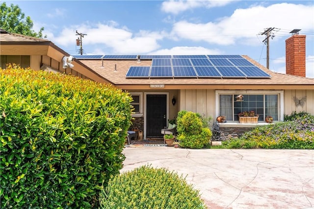19264 Casmalia St, Rialto, CA 92377 - entrance to property featuring a chimney, solar panels, a shingled roof, and board and batten siding