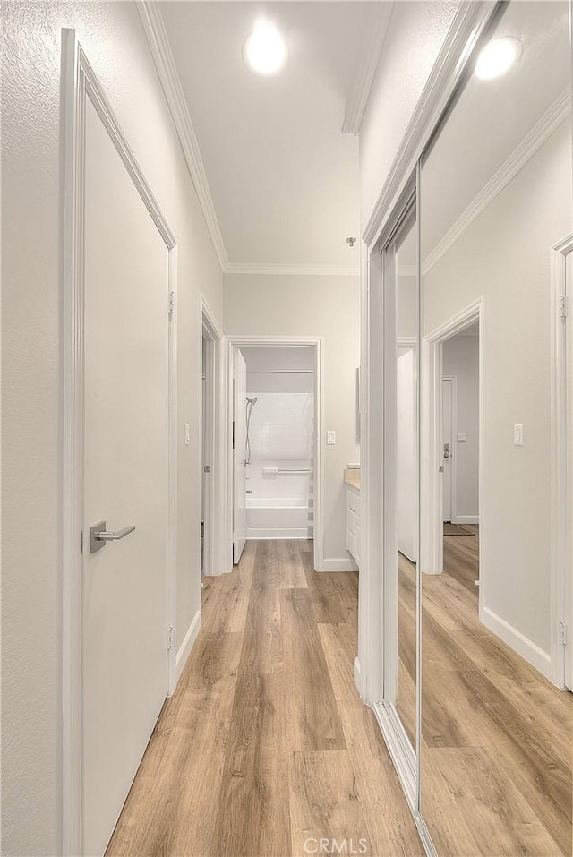 corridor with ornamental molding, light wood-type flooring, and baseboards