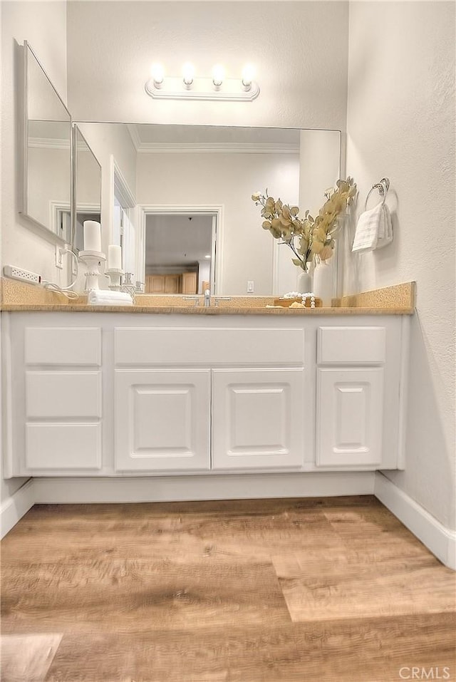 bathroom with crown molding, vanity, wood finished floors, and baseboards