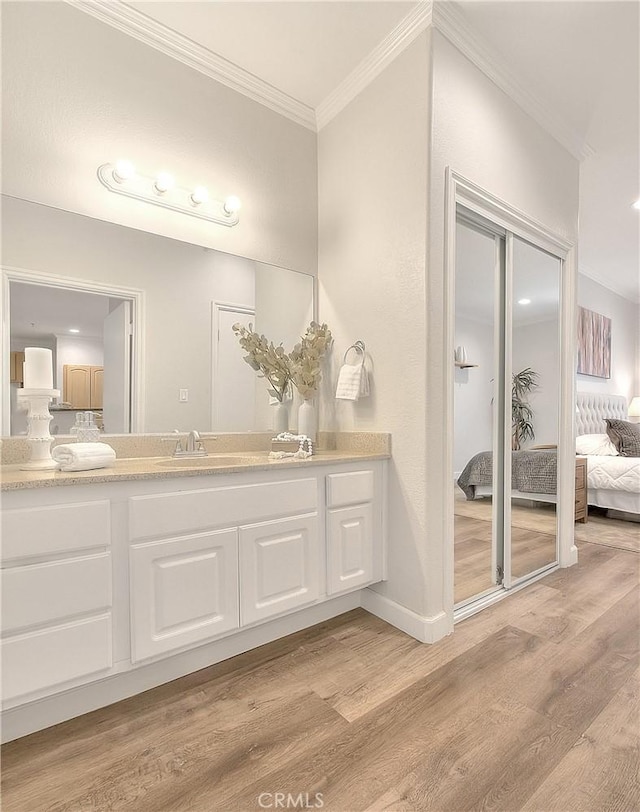 ensuite bathroom featuring wood finished floors, ornamental molding, vanity, and baseboards