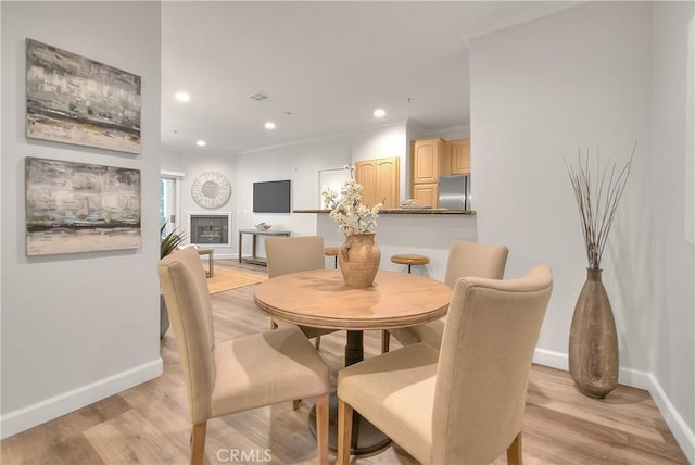 dining area featuring baseboards, recessed lighting, light wood-type flooring, a fireplace, and crown molding