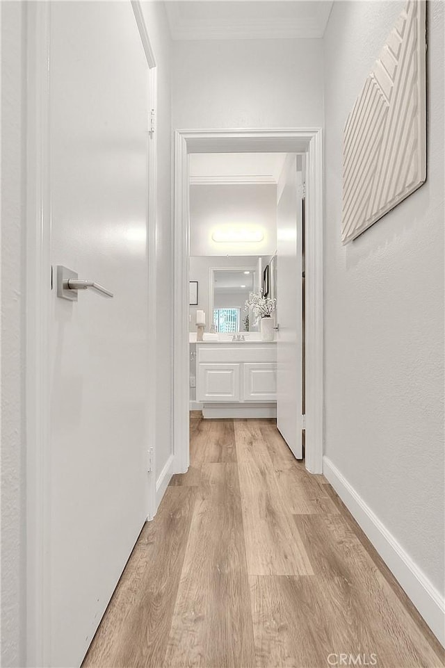 hall featuring light wood finished floors, ornamental molding, and baseboards