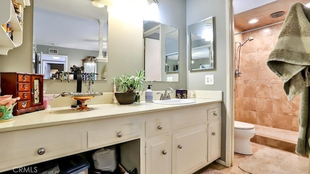 bathroom with a tile shower, toilet, and vanity