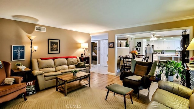 living area with light wood-type flooring, crown molding, ceiling fan, and baseboards