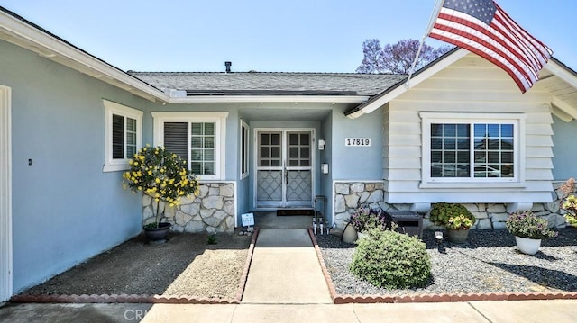 view of exterior entry with stone siding and a shingled roof