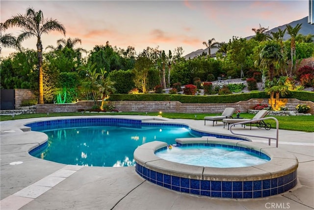 pool at dusk featuring a patio and a pool with connected hot tub