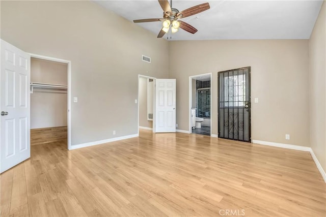 unfurnished bedroom featuring baseboards, light wood-style flooring, a spacious closet, connected bathroom, and high vaulted ceiling