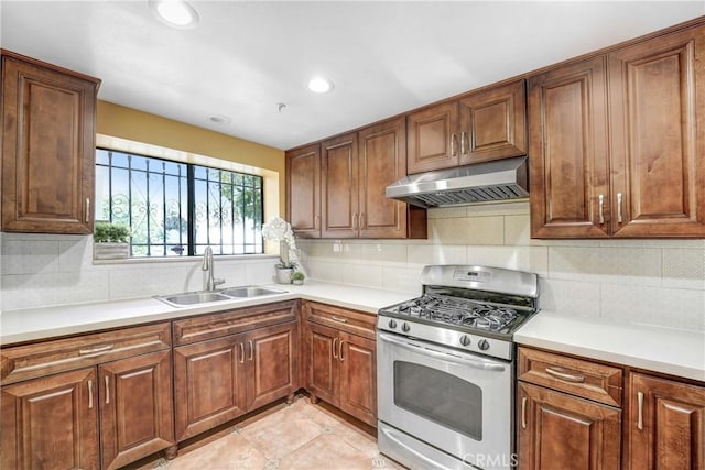 kitchen with stainless steel gas range oven, under cabinet range hood, a sink, backsplash, and light countertops