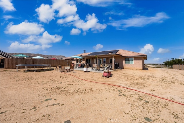 10779 Mills Rd, Apple Valley, CA 92308 - rear view of property featuring a trampoline, a patio, roof mounted solar panels, a fenced backyard, and stucco siding