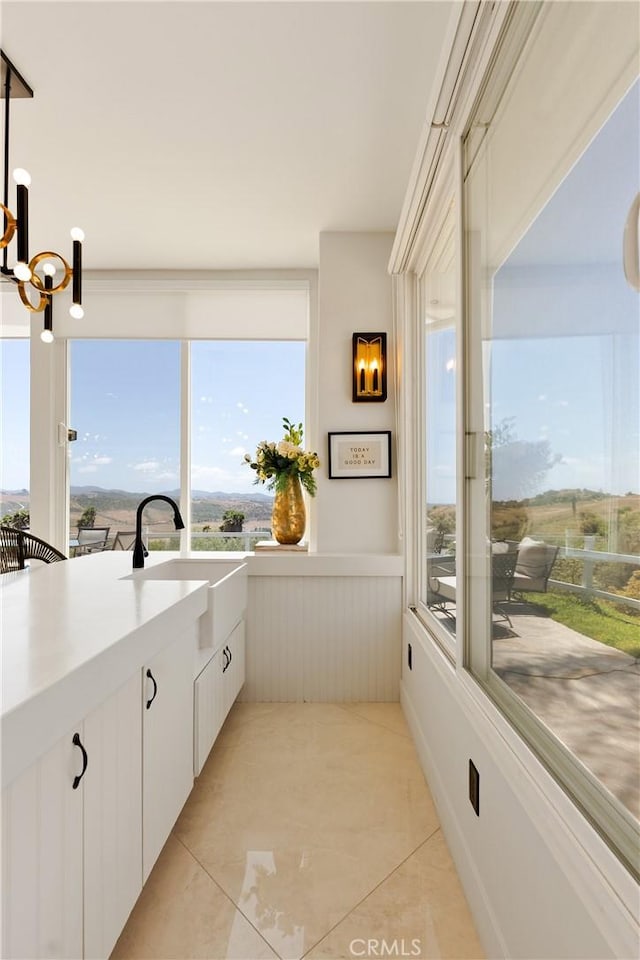 3610 Monserate Hill Ct, Fallbrook, CA 92028 - kitchen with a sink, a wainscoted wall, white cabinetry, light tile patterned flooring, and hanging light fixtures