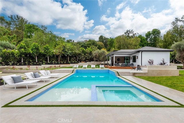 view of swimming pool featuring a patio, a pool with connected hot tub, and view of wooded area
