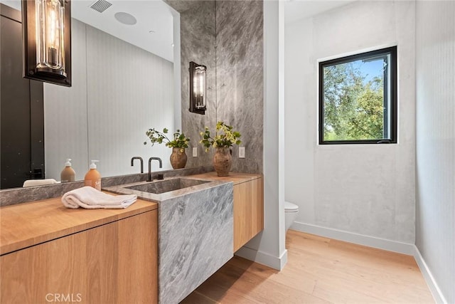 bathroom with wood finished floors, vanity, toilet, and baseboards