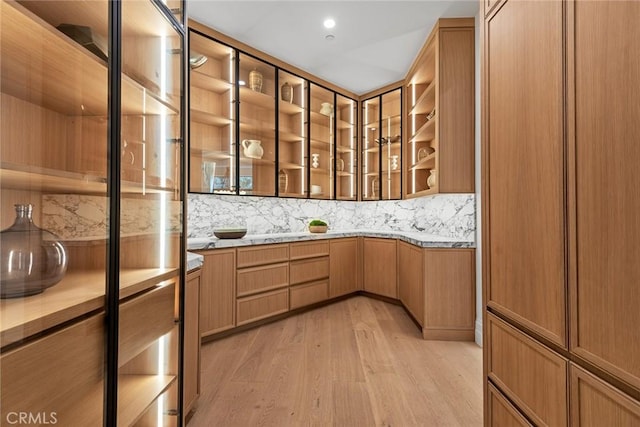 kitchen featuring light wood-style floors, decorative backsplash, open shelves, light countertops, and glass insert cabinets