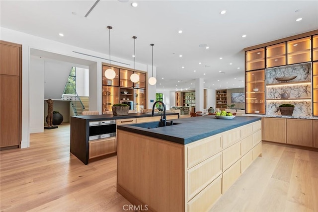 kitchen featuring dark countertops, a large island, a sink, light wood-style floors, and recessed lighting