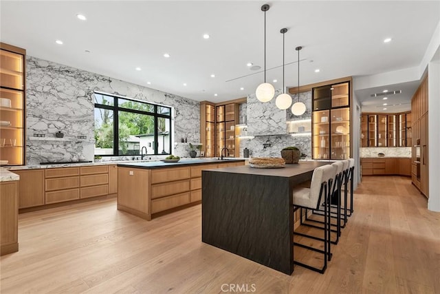 kitchen featuring a large island, light wood finished floors, glass insert cabinets, a sink, and recessed lighting
