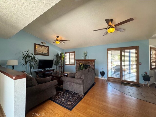 7446 Bangor Ave, Hesperia, CA 92345 - living room with a brick fireplace, a ceiling fan, vaulted ceiling, light wood-style floors, and baseboards