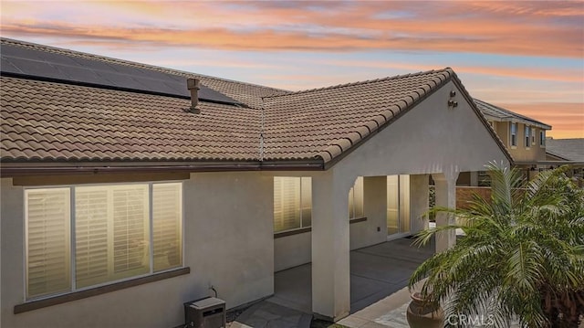 6125 Coopers Hawk Dr, Jurupa Valley, CA 91752 - back of property at dusk with stucco siding, a tiled roof, solar panels, and a patio area