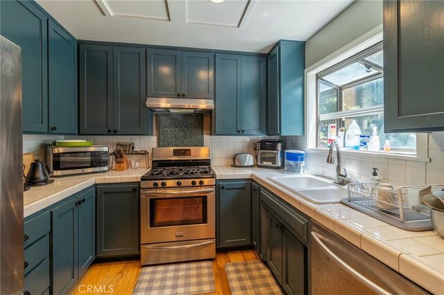 31045 Valley Oak Dr, Running Springs, CA 92382 - kitchen featuring appliances with stainless steel finishes, tile countertops, under cabinet range hood, a sink, and light wood-style flooring