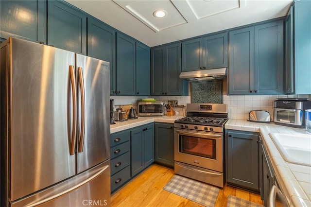 31045 Valley Oak Dr, Running Springs, CA 92382 - kitchen featuring appliances with stainless steel finishes, tile counters, under cabinet range hood, and light wood-style floors