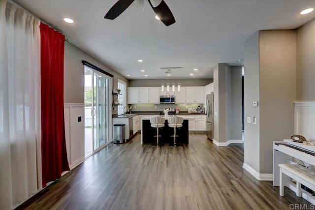 29567 Castlewood Dr, Menifee, CA 92584 - kitchen featuring stainless steel appliances, a ceiling fan, wood finished floors, white cabinets, and a wainscoted wall