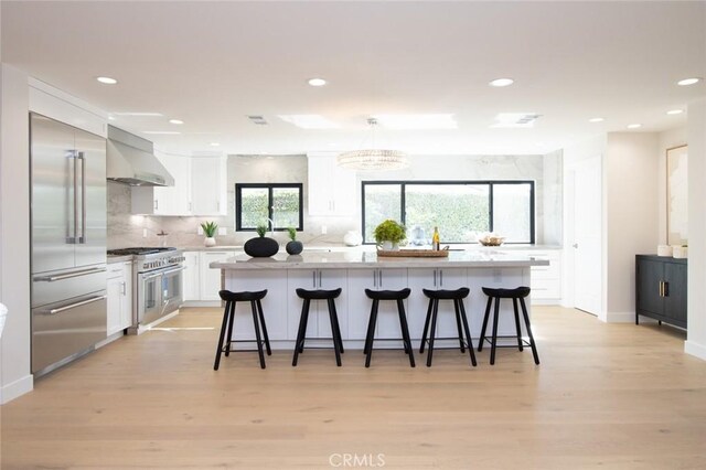 12312 Eveningside Dr, Santa Ana, CA 92705 - kitchen featuring wall chimney exhaust hood, high quality appliances, light wood-type flooring, white cabinets, and recessed lighting