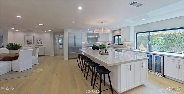 12312 Eveningside Dr, Santa Ana, CA 92705 - kitchen with wall chimney range hood, stainless steel appliances, white cabinetry, a kitchen bar, and a center island