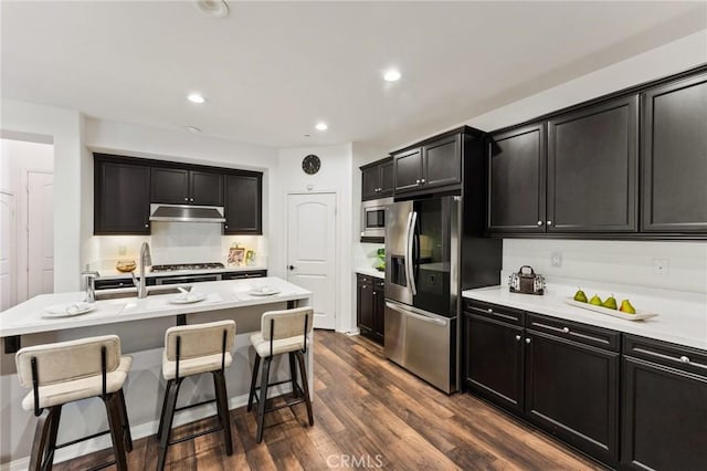 2974 E Walking Beam Pl, Brea, CA 92821 - kitchen with appliances with stainless steel finishes, under cabinet range hood, a breakfast bar, dark cabinets, and dark wood finished floors