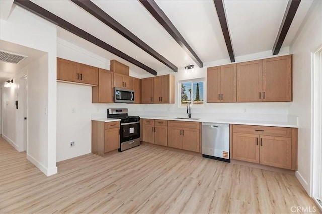 kitchen with appliances with stainless steel finishes, a sink, light wood-style floors, and light countertops