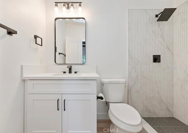 bathroom with a tile shower, vanity, toilet, and baseboards