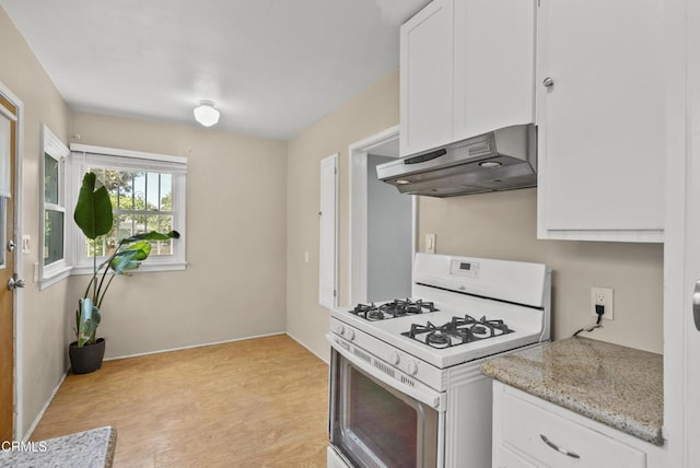 kitchen featuring under cabinet range hood, white gas range, white cabinetry, light wood-style floors, and light stone countertops
