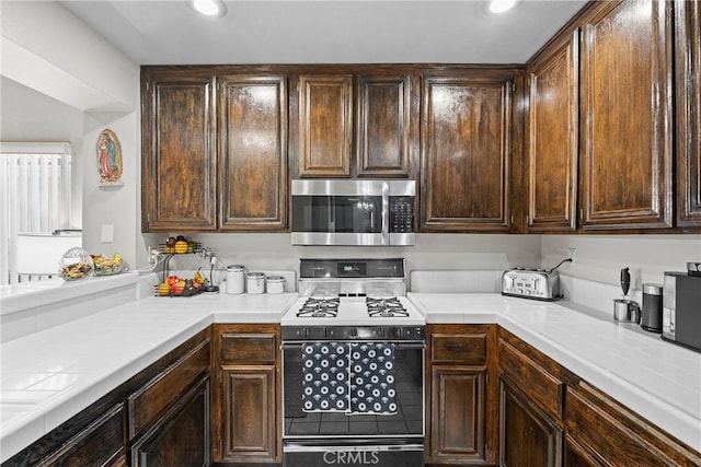 4856 W Glen Abbey Way, Banning, CA 92220 - kitchen featuring stainless steel microwave, range with gas cooktop, dark brown cabinets, recessed lighting, and tile counters