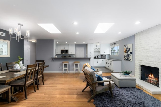 3696 Ben St, San Diego, CA 92111 - living room with a skylight, a chandelier, light wood-style flooring, a brick fireplace, and recessed lighting
