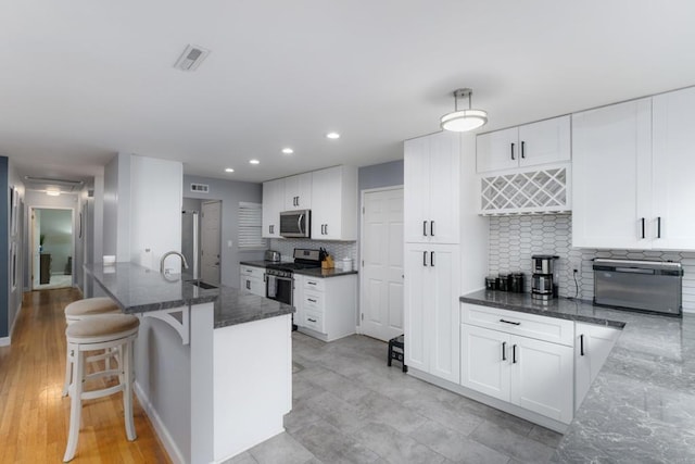 3696 Ben St, San Diego, CA 92111 - kitchen with stainless steel appliances, dark stone counters, tasteful backsplash, white cabinetry, and a breakfast bar