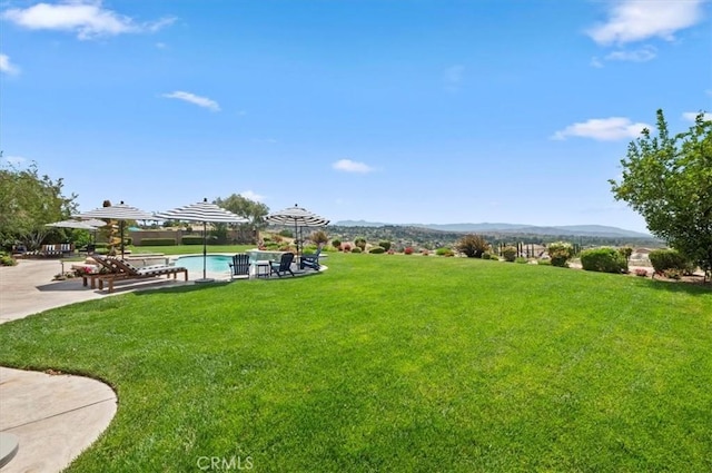 view of green lawn with an outdoor pool, a mountain view, and a patio area
