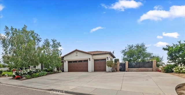mediterranean / spanish-style home with concrete driveway, an attached garage, stucco siding, a tiled roof, and a gate
