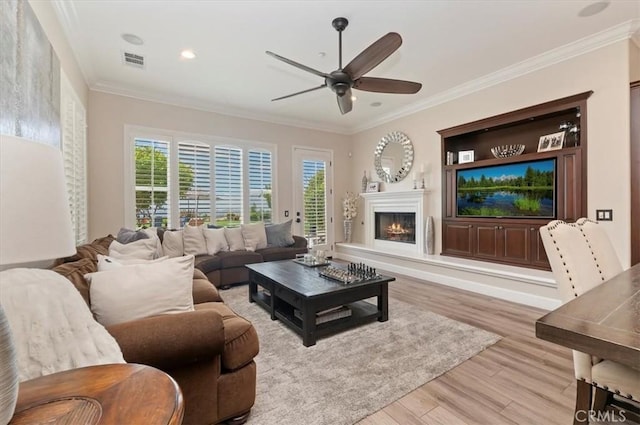 living area with a ceiling fan, wood finished floors, ornamental molding, a warm lit fireplace, and recessed lighting