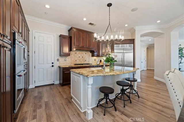 kitchen with stainless steel appliances, light stone counters, a kitchen breakfast bar, light wood-type flooring, and backsplash