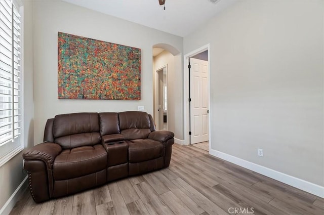 living area featuring arched walkways, light wood finished floors, and baseboards