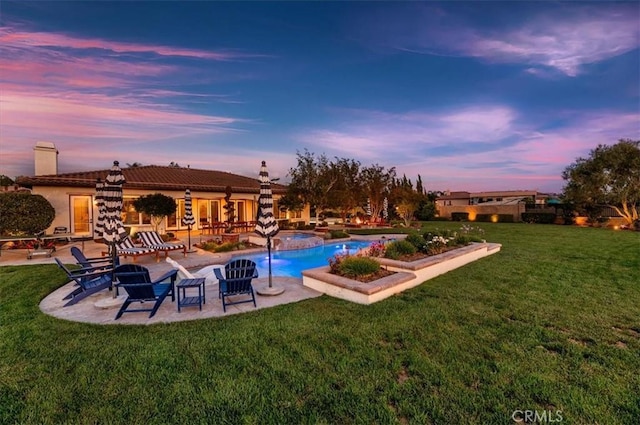 pool at dusk with a patio area, a yard, and a pool with connected hot tub
