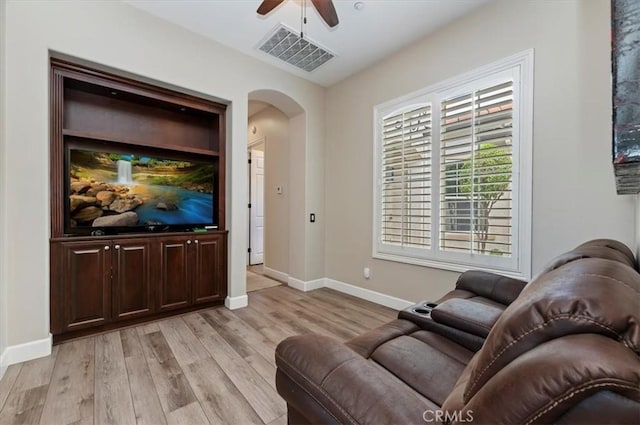 living area with arched walkways, ceiling fan, light wood-style flooring, and baseboards