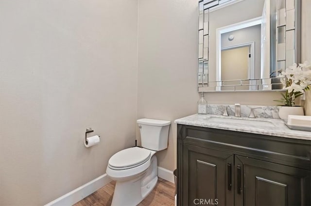 half bathroom with baseboards, toilet, wood finished floors, and vanity