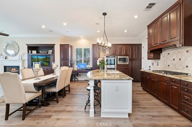kitchen with appliances with stainless steel finishes, a chandelier, light wood finished floors, light stone counters, and a kitchen bar