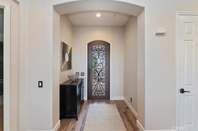 foyer with arched walkways, light wood-type flooring, and baseboards