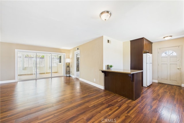 kitchen featuring freestanding refrigerator, dark wood-style floors, a kitchen breakfast bar, light stone countertops, and open floor plan