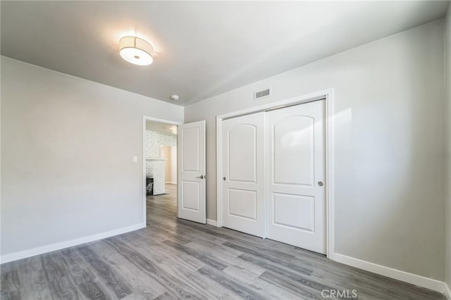 unfurnished bedroom featuring baseboards, wood finished floors, a closet, and a brick fireplace